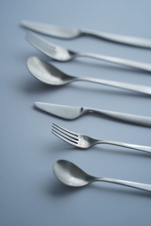 vertical high angle closeup shot of forks, spoons, and knives on grey background